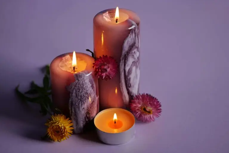 Three candles burning warmly surrounded by flowers on a purple surface.